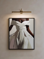 Framed abstract artwork of a white dress on a beige wall with a gold light fixture.