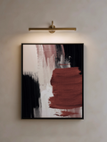 Abstract art piece with red, black, and white brush strokes in a black frame, illuminated by a wall-mounted light fixture.