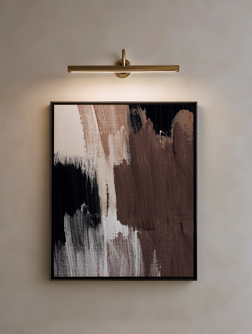 Abstract art piece with brown, black, and white brushstrokes in a black frame, illuminated by a wall-mounted light fixture.