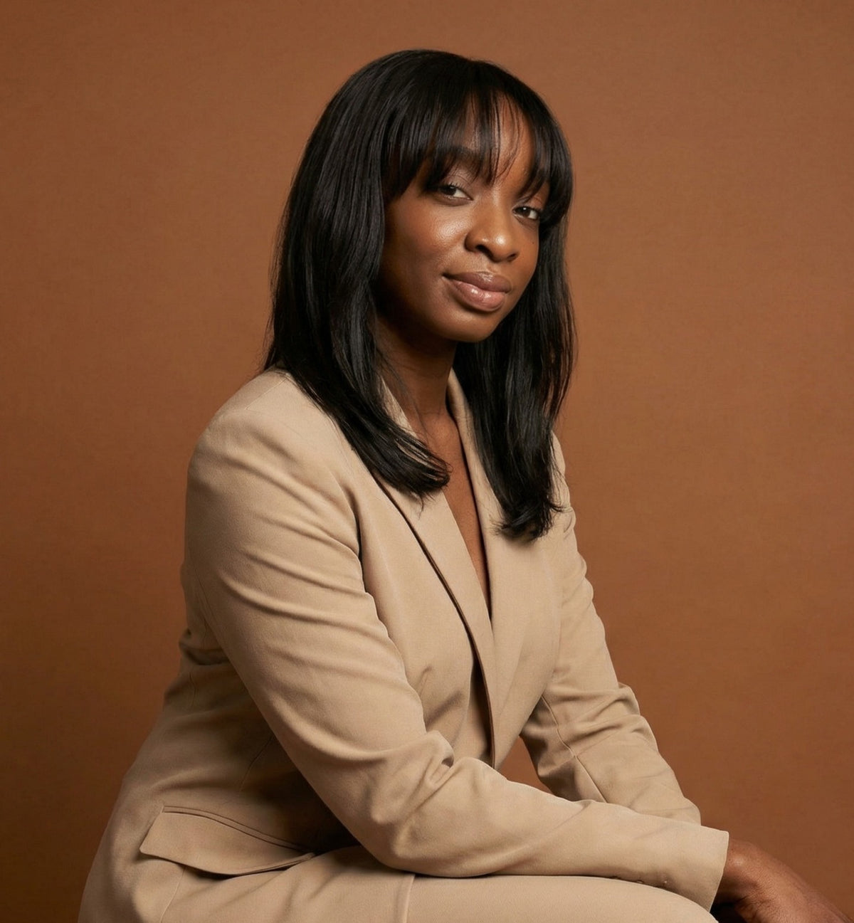 Woman in a beige suit sitting against a brown background. Akua Home Founder