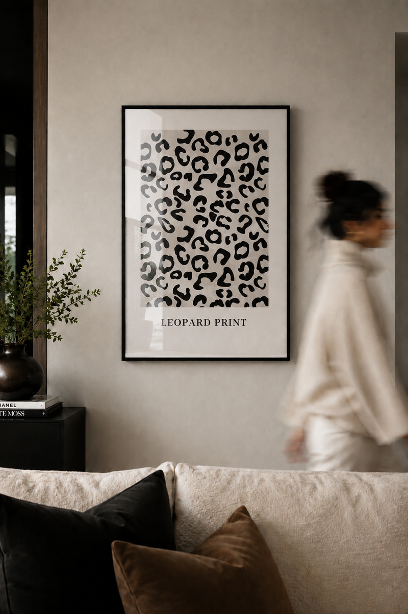 Framed leopard print art on a wall with a person walking by