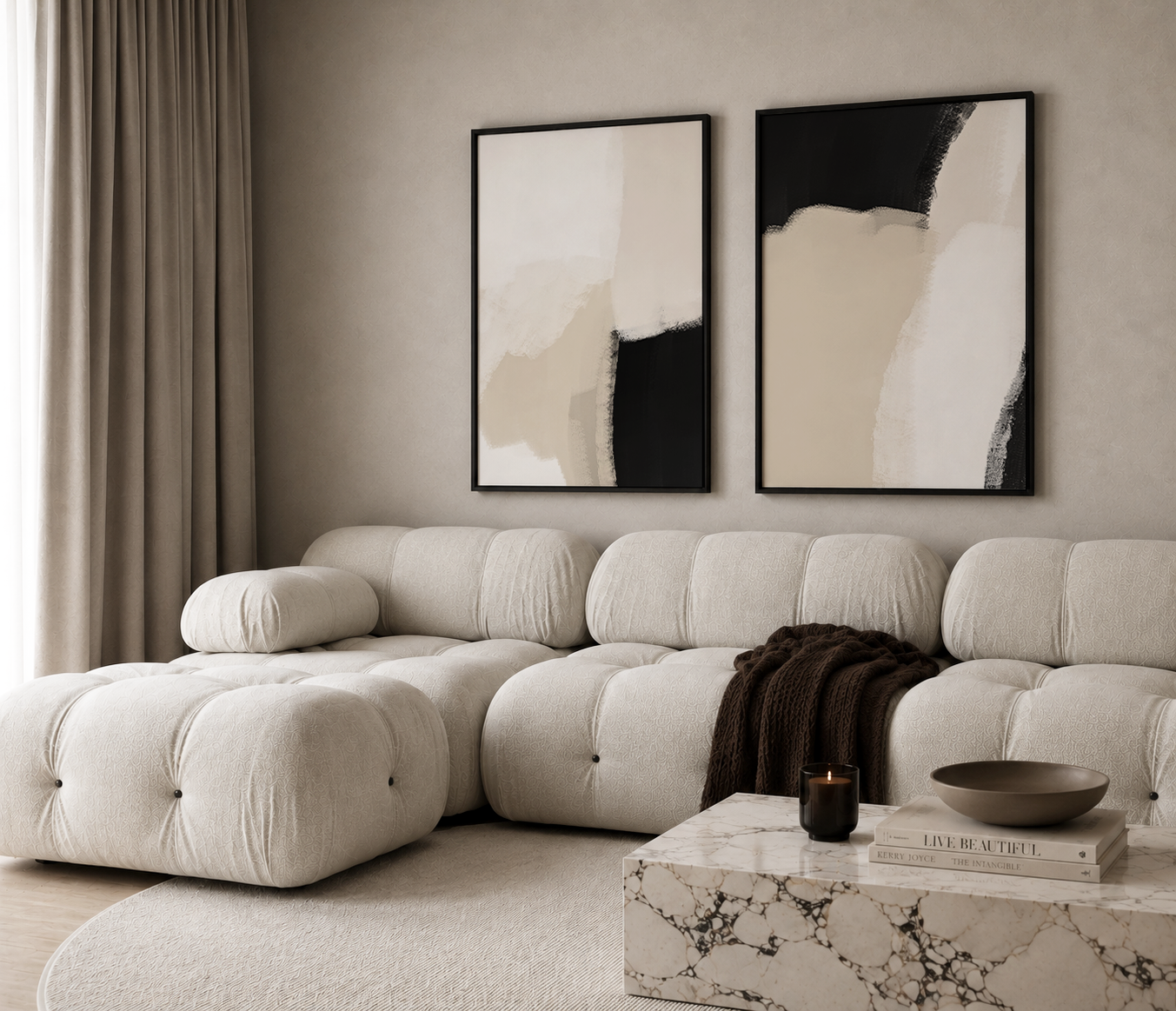 A modern tufted sectional sofa in a warm off-white or cream color, styled in a minimalist living room with two large abstract black, beige, and white framed wall art prints above it. 