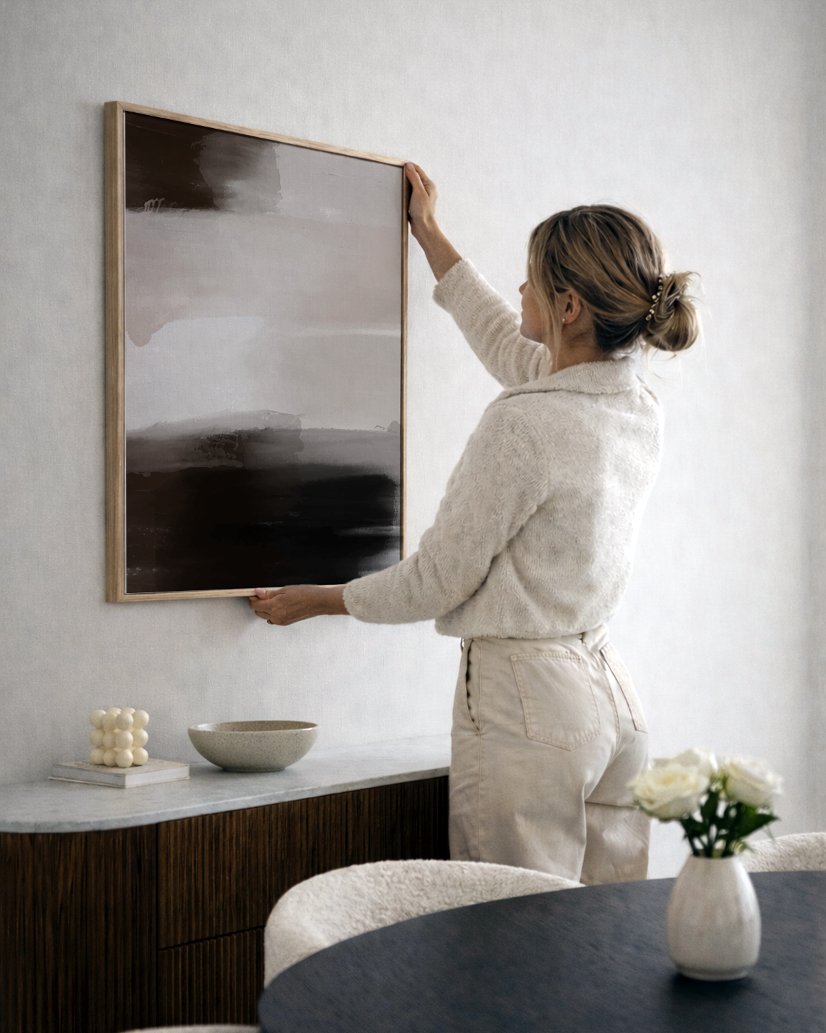 Woman hanging a framed artwork on a wall in a modern interior setting.