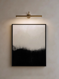 Modern wall light fixture above a framed abstract neutral and black artwork on a neutral wall.